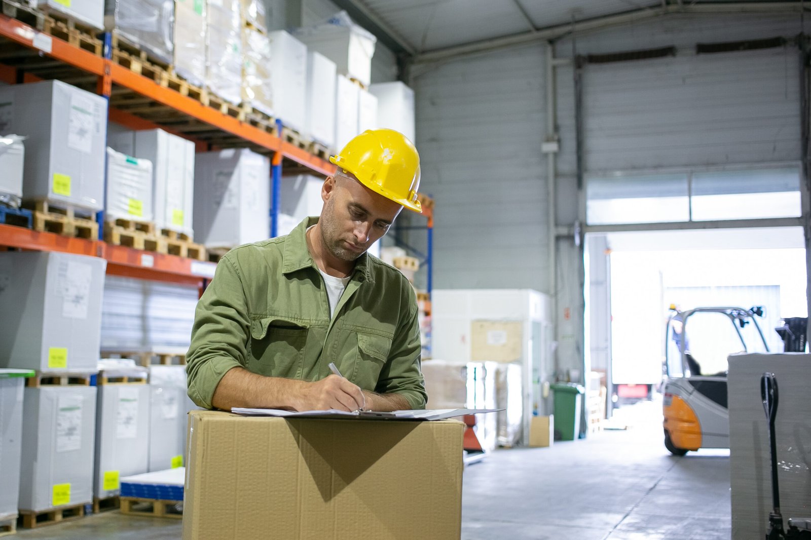 Serious Male Logistic Engineer Hardhat Overall Standing Stack Boxes Completing Documents Copy Space Blue Collar Labor Concept Scaled